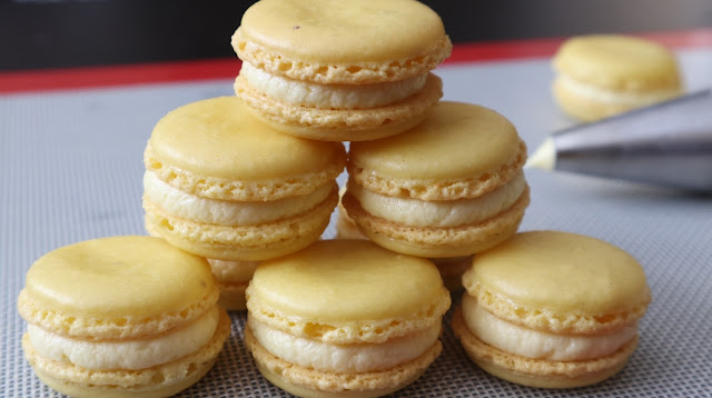 Lemon Macarons in a pyramid on a silicon mat. Lemon buttercream piping bag in background with a lemon macaron