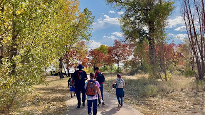 5 CCB students walking on a trail through trees whose leaves have changed from green to yellow and red