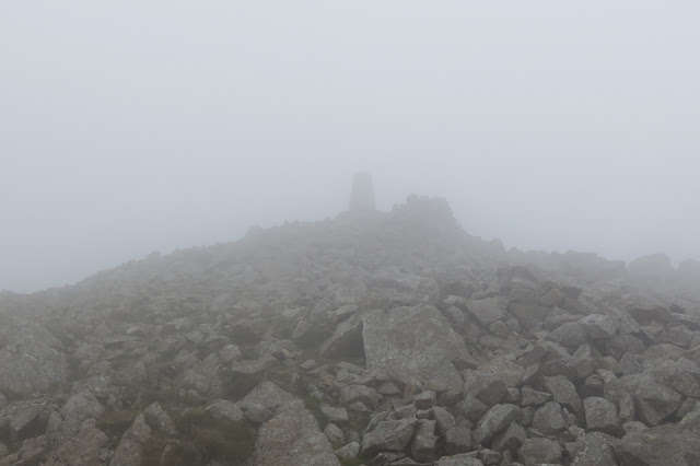 Just visible on a crown of rocks, the OS trig in mist at the summit.