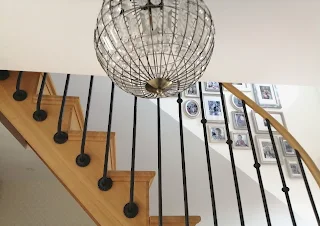 vue d'ensemble sur le luminaire de l'entrée, l'escalier en chêne avec rambarde en fer forgé