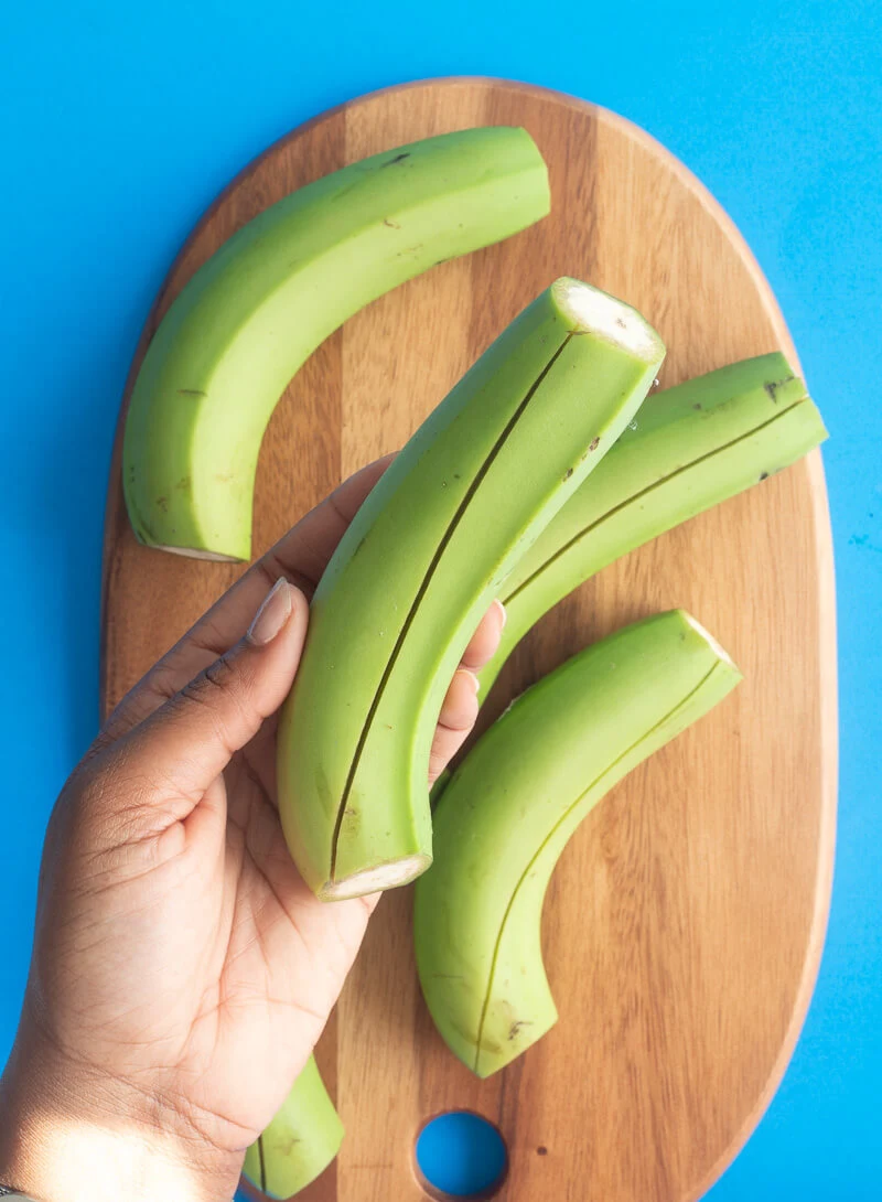 A green banana with a slit from the top to the bottom showing how to pierce the skin to boil.