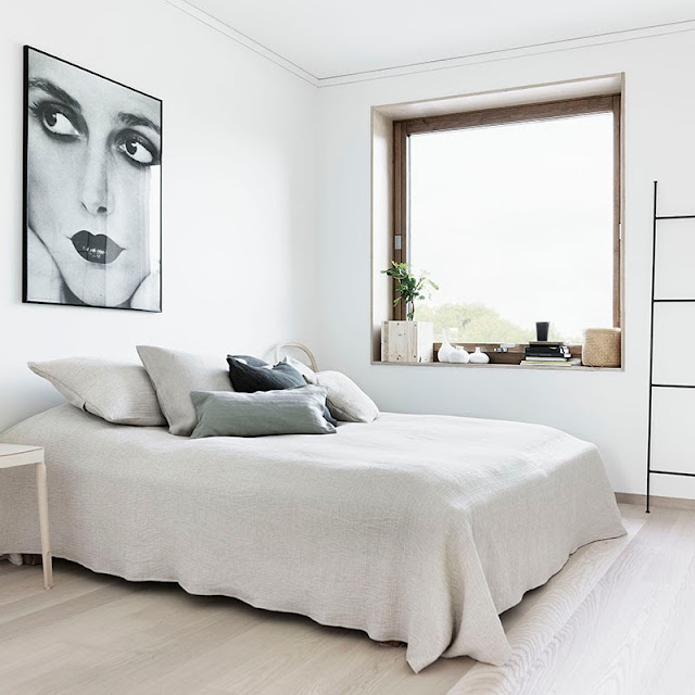 Clean white bedroom with light wood floor, a large window and a framed portrait
