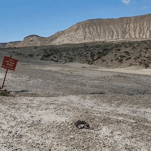 A dry, cracked landscape in Gobustan with a red sign marking it as a state-protected ancient reserve, restricting public access to preserve the site.