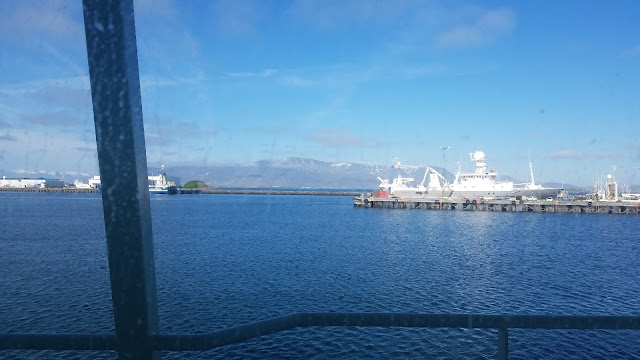 Picture shows shipping pier with a docked ship and a mountain in the far background. Slight haze is visible over entire image, as it was taken through the window of the ship. 