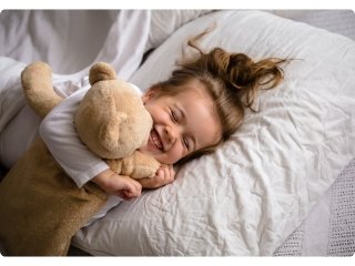 A little girl snuggles with her favorite teddy bear during bedtime, hugging it tightly for comfort.