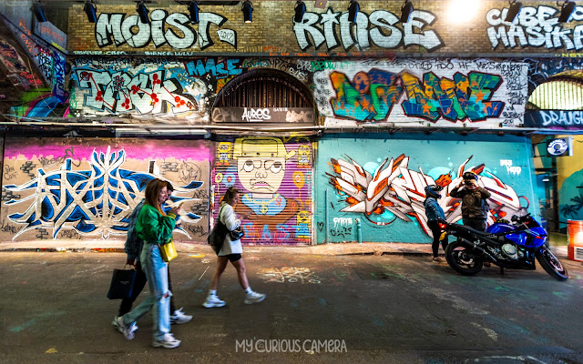 Graffitied London tunnels showing people walking and a motorcyclist by his motobike chatting with a friend