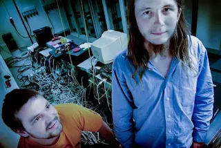 Dois hackers em meio a computadores e cabos de rede.