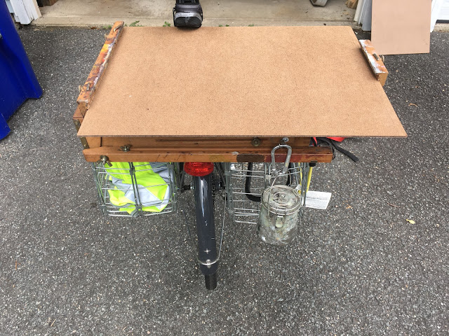 Bicycle carrying french easel and large panel on top of rear pannier baskets