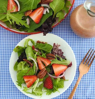 overhead shot of strawberry salad on a white plate with bottle of dressing