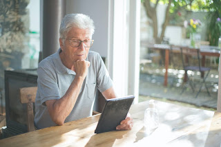 A photo of an elderly man looking at a tablet.