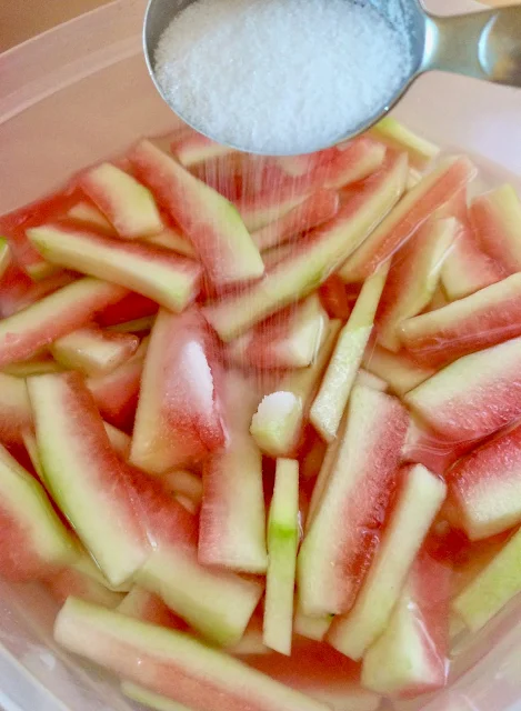 Pouring sugar into a bowl of watermelon rinds and water.