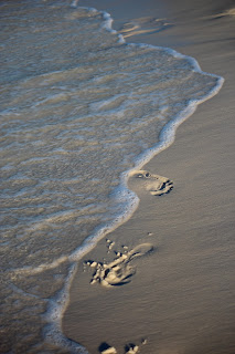 Waves washing away footprints in the shore along Pensacola Beach, FL