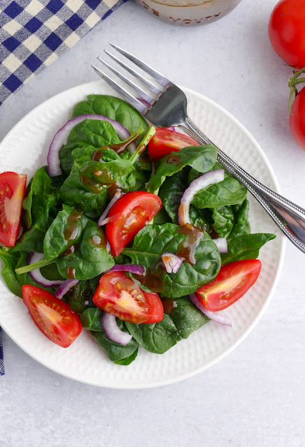 spinach salad on a white plate with dressing on top.