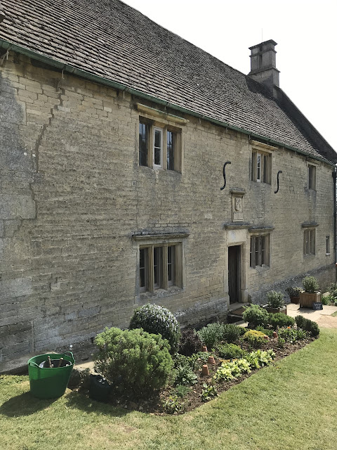 Exterior of a stone manor house, with tidy and flower boarders in front of the house