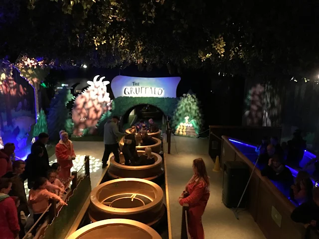 A river with round boats which are being filled up with people in the queue by staff wearing orange jumpsuits.