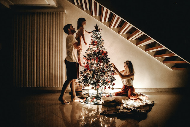 Mamá, papá e hija decorando el árbol de Navidad.