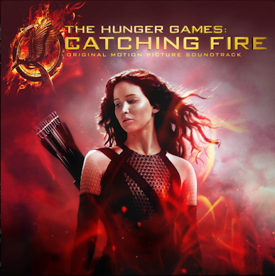 The Hunger Games: Catching Fire soundtrack album cover. Katniss Everdeen, the heroine of the series, a young woman with long brown hair, looks downwards while wearing a warrior's outfit, a bow and arrow set, and surrounded by a dark red background, fiery, simulating flames.