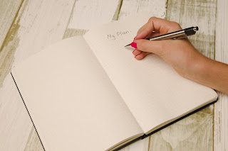 A hand preparing to write the design for a game on a page in a notebook that has the words 'My Plan' written across the top.