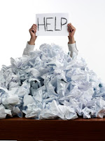 pile of scrunched up paper on a desk and a sign saying "help" 