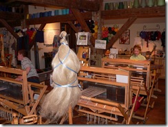 Children  (mostly boys) being taught how to weave on looms.  Flax is waiting to be spun into yarn in foreground.