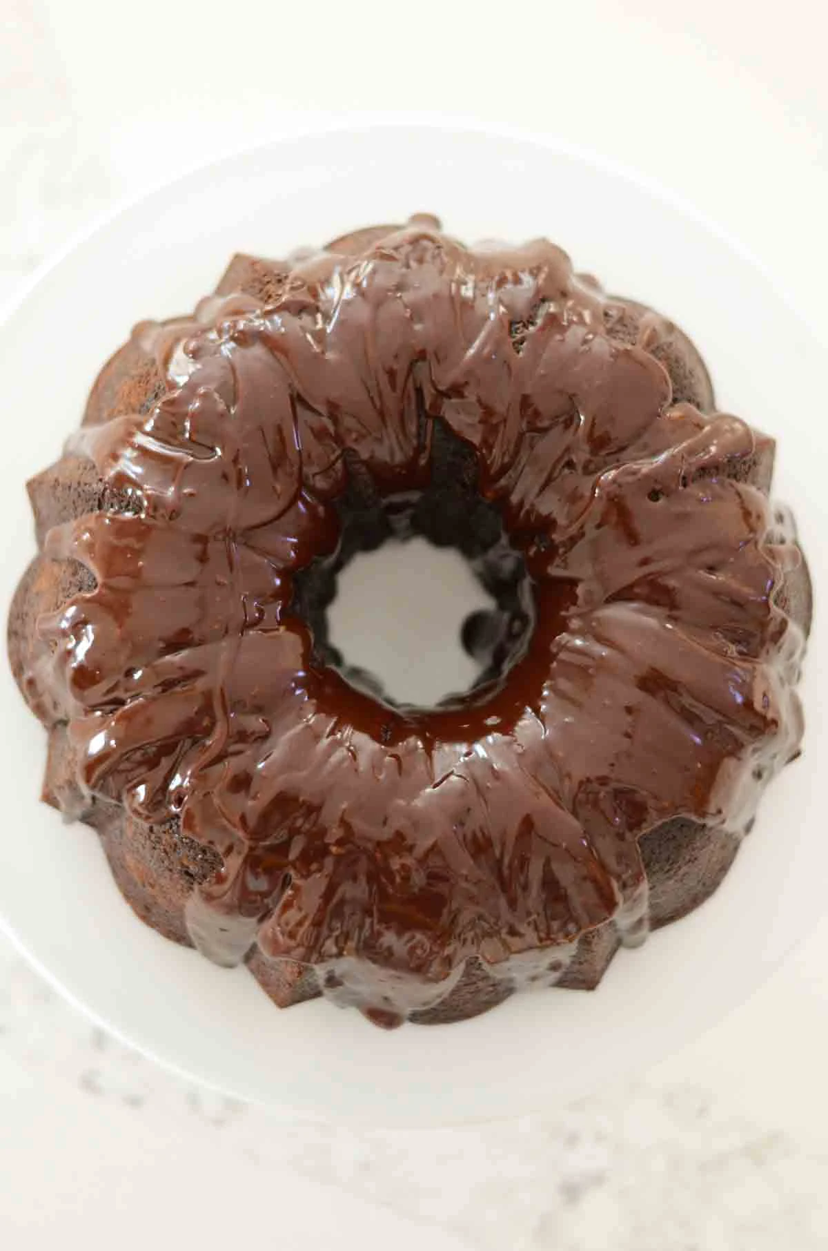 A down shot of a Chocolate Bundt Cake covered with Chocolate Glaze on a white cake pan.