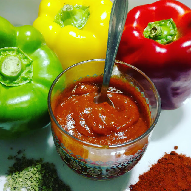 En la imágen vemos una salsa barbacoa casera rodeada de parte de los ingredientes utilizados en su cocinado: Orégano, pimentón y pimientos de tres colores (amarillo, rojo y verde) comprados en el MERCADONA