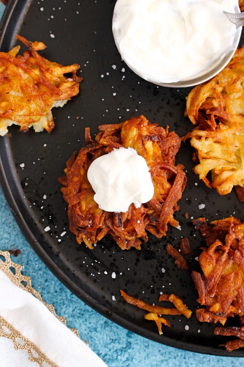 Crispy Polish Potato Pancakes on a black plate with a blue table with a dollop of sour cream on top.