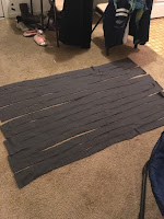 A yard of dark grey fleece laid out on a carpeted floor, cut into long strips connected at the very ends.