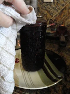 Cleaning rim of canning jar filled with blackberry jam with a damp cloth.