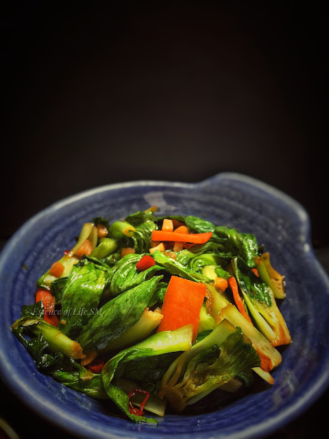 A colorful stir-fry dish featuring vibrant green bok choy and sliced carrots, seasoned with garlic and oyster sauce.