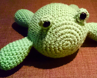 Crochet frog plushie made with acrylic yarn in pale green. The design is different to the others, the body an oval shape with floppy limbs out the sides with to little nubbins for eyes, with safety button eyes attached.