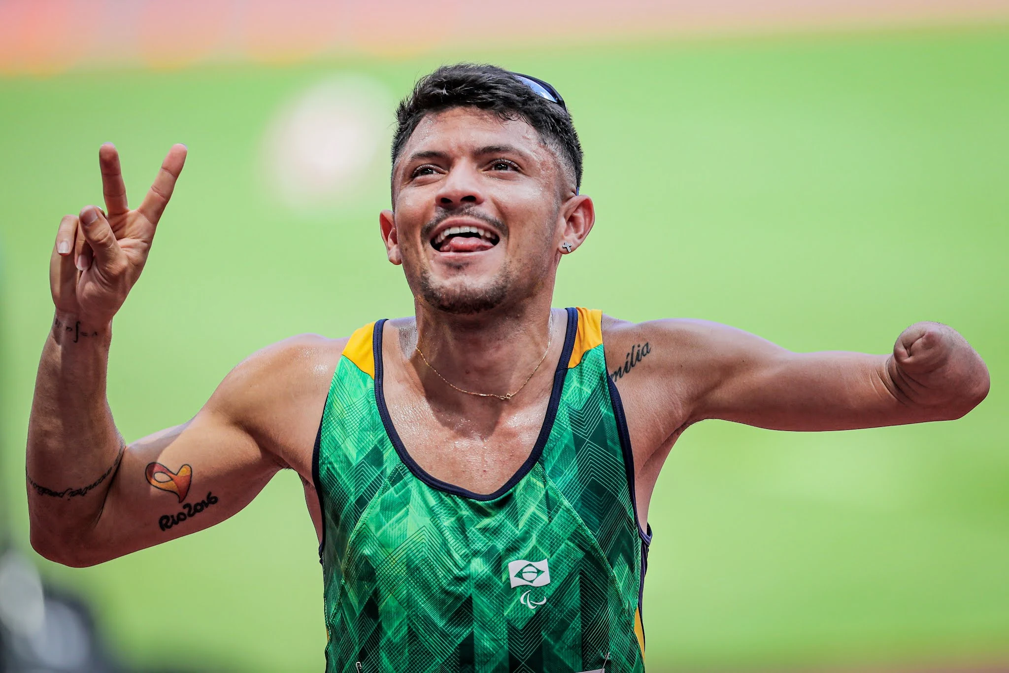 Petrúcio Ferreira, de uniforme verde, sorri e mostra a tatuagem no muque esquerdo