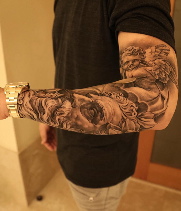 Bem detalhada manga tatuagem, você pode ver uma estátua que se assemelha a um jovem anjo. Abaixo dele é outra imagem que é um rosto de um homem com cabelos longos e barba, que também é uma estátua esculpida em si.  