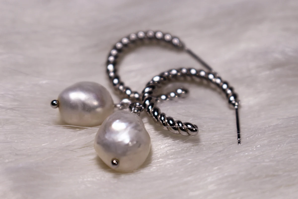 studio close-up of two silver earrings with white pearls on white background