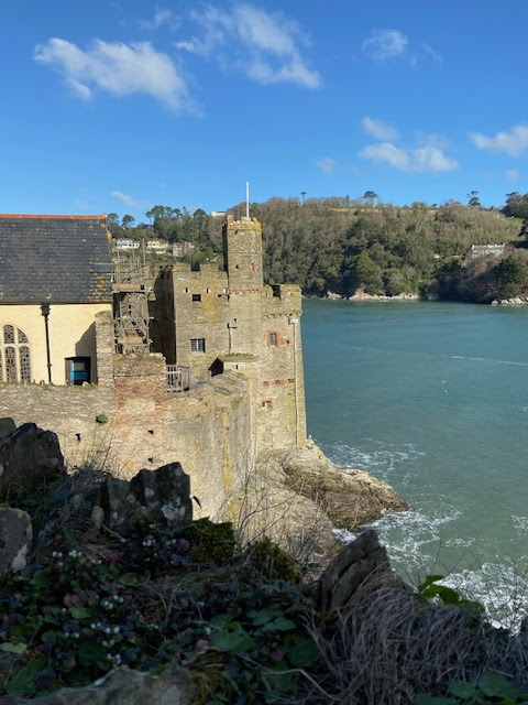 The medieval part of Dartmouth Castle in the sunshine, standing on rocks with the sea crashing below.