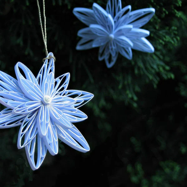 Two Quilled Snowflake Ornaments hanging on green foliage