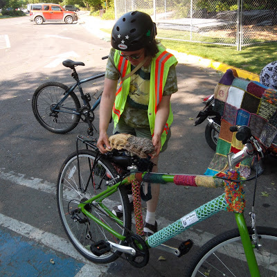 Cynthia Parkhill places knit-swatch seat cover on yarn-bombed bicycle