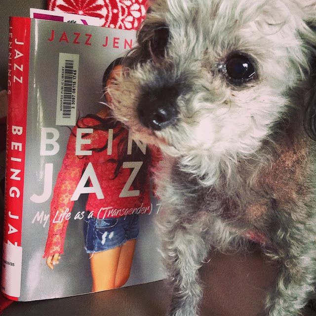 Murchie stares mournfully upwards as he stands beside a hardcover copy of Being Jazz. The book's cover features a photo of a happy, brown-skinned girl wearing denim shorts and a long-sleeved pink lace top.