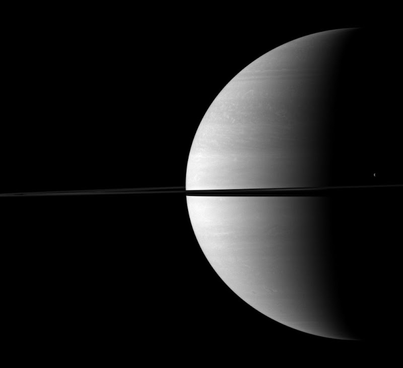 The moon Tethys stands out as a tiny crescent of light in front of the dark of Saturn's night side.