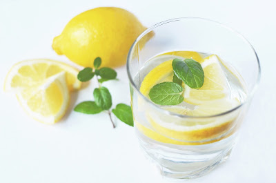 Full glass of water with lemon and mint, with whole lemon, lemon slices, and sprig of mint next to it