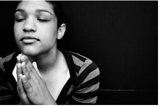 Photo of a young black woman praying with her eyes closed and hands together