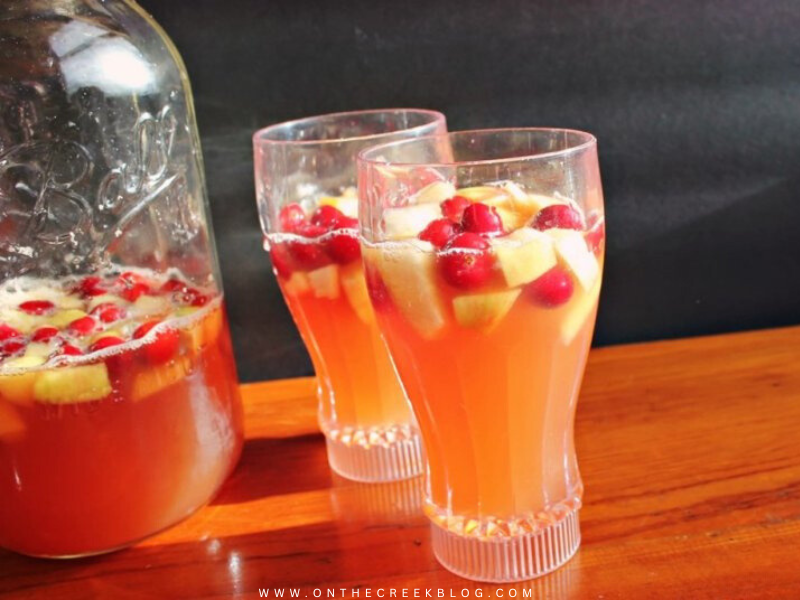 Caramel Apple Punch in a glass pitcher, garnished with fresh-cut apples and cranberries, perfect for fall gatherings. | on the creek blog // www.onthecreekblog.com