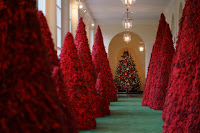 Large Christmas trees completely covered in red cranberries on a green carpet with a traditional Christmas tree in the background. This is in the White House.