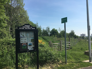 A black board with a sign that says Little France Park with grass behind it.