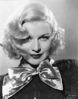Ginger Rogers with short wavy blonde hair wearing a dark button up shirt and a huge silver bow at the collar.