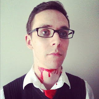 Josh, wearing a waistcoat, collared shirt and tie, staring vacantly into the middle distance, with his throat slashed.