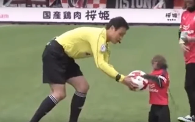 A monkey mascot dressed in full Cerezo Osaka kit hands over the match ball to referee Hiromu Kimura