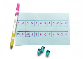 na zdjęciu plansza do gry namalowana odręcznie, obok planszy leży pisak oraz trzy kostki w kolorze błękitny,