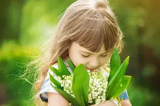 Young girl with blonde hair standing in a field of wildflowers, hugging a bouquet of flowers and smelling them with a pleased expression.