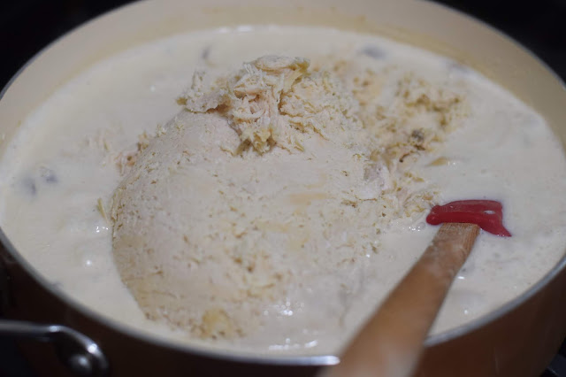 Shredded chicken added to the pan of sauce on the stove. 